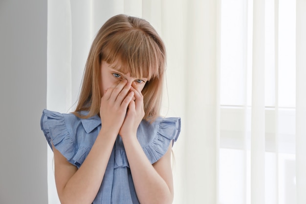 Petite fille triste près de la fenêtre à la maison