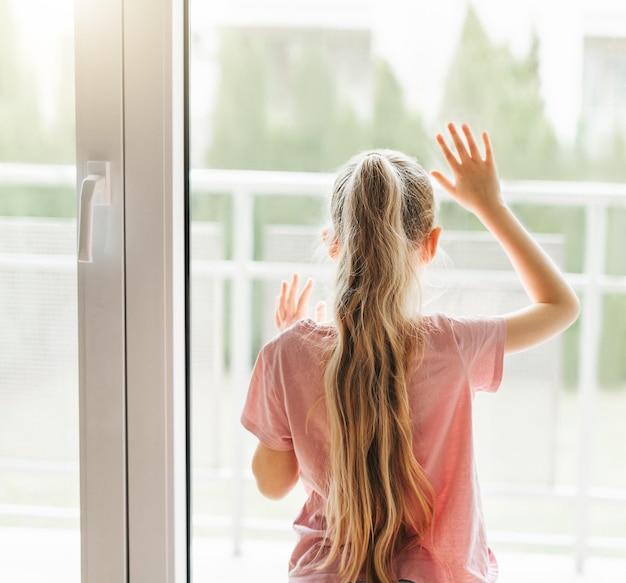 Une petite fille triste regardant par la fenêtre à la maison.