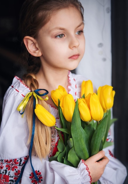 Une petite fille ukrainienne en vêtements traditionnels tient une tulipe jaune dans ses mains