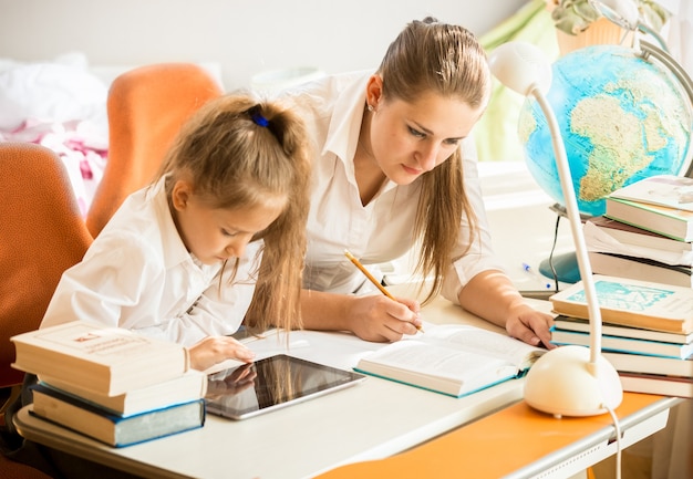 Petite fille utilisant une tablette numérique pendant que sa mère fait ses devoirs à sa place