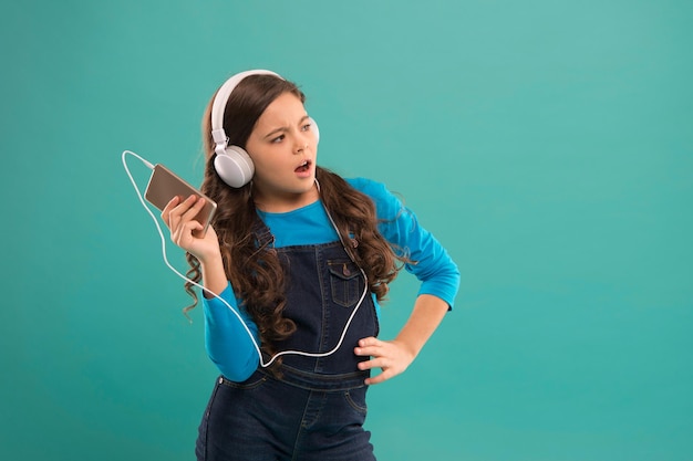 Petite fille utilise un lecteur mp3 étude dans la vie moderne écolière utilise un appareil numérique mode décontractée pour les enfants enfant cheveux longs écouter de la musique dans le casque petit enfant faire une liste de lecture sur l'espace de copie du smartphone