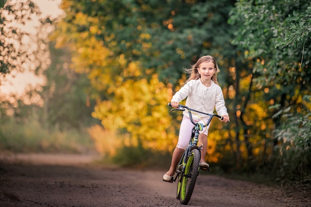 Petite fille va avec un vélo sur une route rurale dans la nature au coucher du soleil