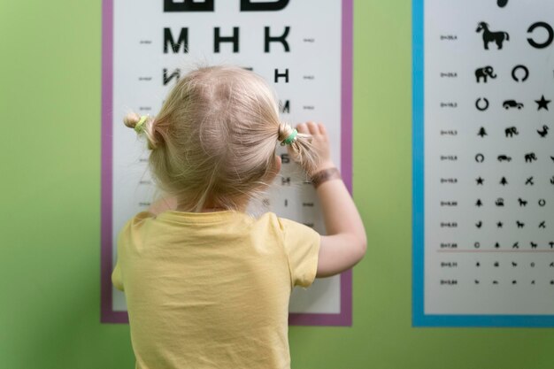 Une petite fille vérifie sa vue lors d'un rendez-vous avec un optométriste Une fille regarde l'affiche de Sivtsev Examen de la vue chez les enfants