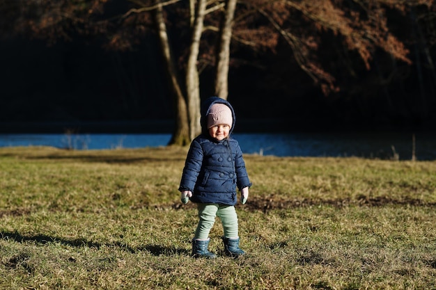 Petite fille en veste debout dans un parc de printemps ensoleillé contre la rivière