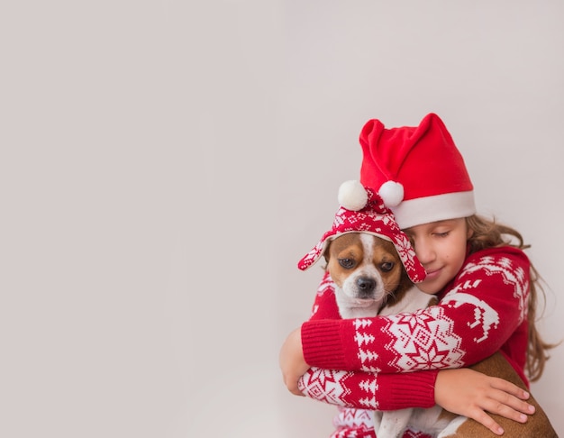 Petite fille en veste de Noël et chapeau tenant petit chien en chapeau d'hiver