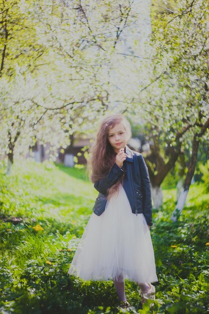 Petite fille en veste noire reniflant une marguerite dans le jardin de cerisiers de printemps