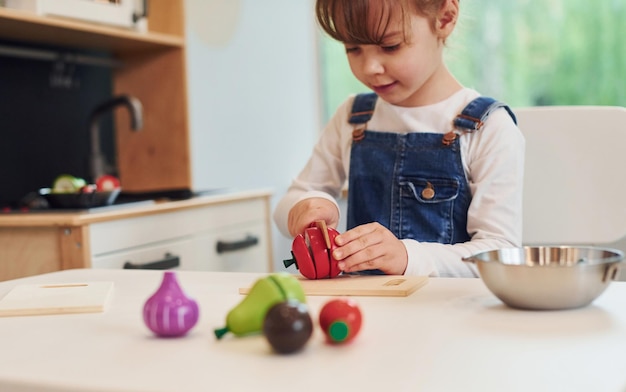 Une petite fille en vêtements décontractés est assise à table et s'amuse en jouant avec des jouets dans la cuisine