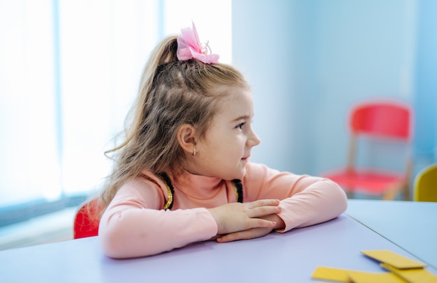 Petite fille en vêtements décontractés en levant et en pensant. Assis à la table.