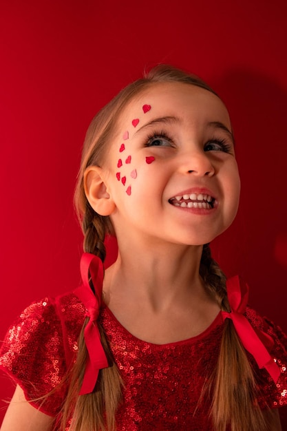 Une petite fille vêtue d'une élégante robe rouge à paillettes sur fond rouge avec des nattes sourit joyeusement