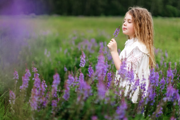 Une petite fille vêtue d'une robe blanche avec de belles fleurs sur le terrain en été