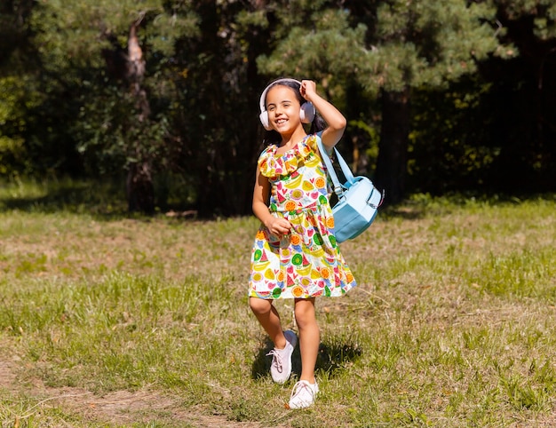 Petite fille vêtue d'une robe et d'un casque s'amuse et saute dans le parc sur l'herbe.