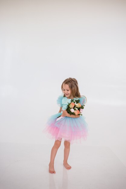 Une petite fille vêtue d'une robe avec une jupe tutu tient un bouquet de fleurs fraîches sur fond blanc avec une place pour le texte