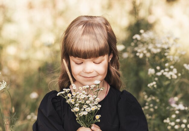 Petite fille vêtue d'une robe noire élégante dans la nature en été avec des fleurs