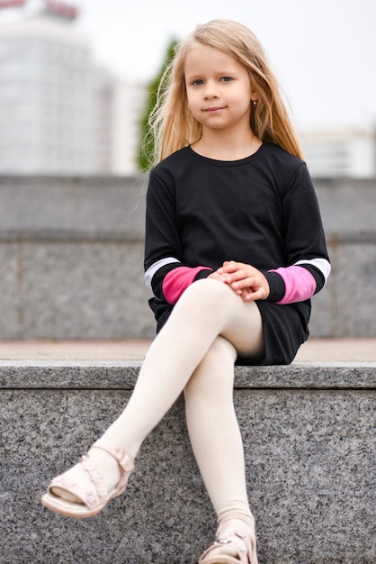 Une petite fille vêtue d'une robe noire est assise sur un banc.