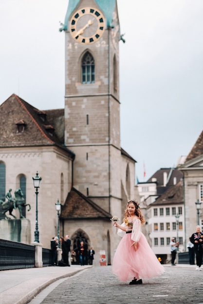 Une petite fille vêtue d'une robe de princesse rose avec un bouquet dans les mains se promène dans la vieille ville de Zurich.Portrait d'une fille vêtue d'une robe rose dans une rue de la ville de Suisse