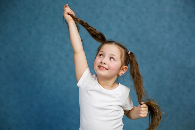 Petite fille vêtue d'un t-shirt blanc et d'un jean s'amusant avec ses cheveux