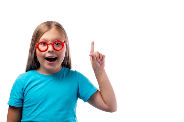 Une petite fille vêtue d'un T-shirt bleu et de lunettes rondes en plastique leva son index. Isolé sur fond blanc. Place pour le texte