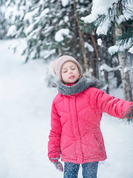 Une petite fille vêtue d'une veste brillante joue dans la forêt enneigée d'hiver.