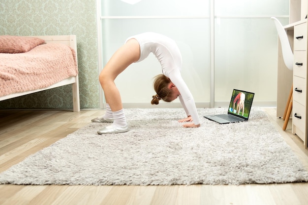 Petite gymnaste en justaucorps blanc à la maison étudiant à distance Cours de gymnastique à domicile Cours de gymnastique en ligne