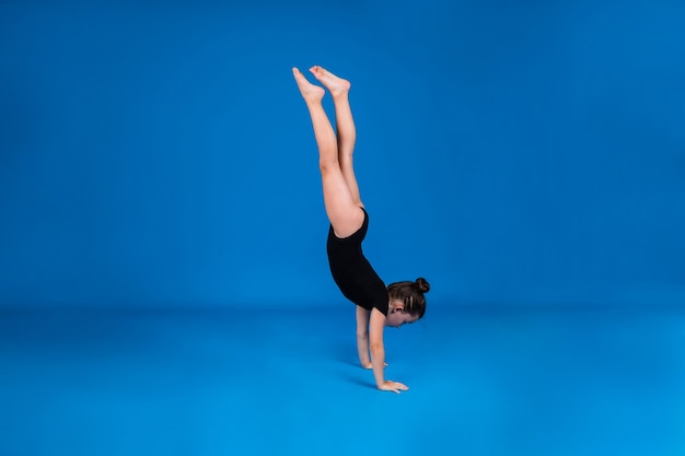 Une petite gymnaste en maillot de bain noir se tient sur ses mains sur fond bleu avec une copie de l'espace