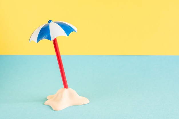 Petite île de sable avec parapluie sur fond bleu pastel