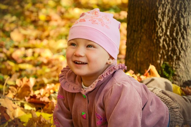 Petite jolie fille allongée sur des feuilles d'érable dans le parc et riant