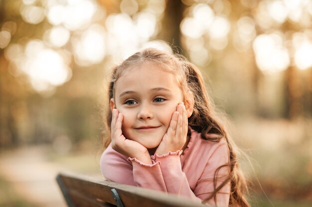 Petite jolie fille assise sur un banc dans le parc à l'automne