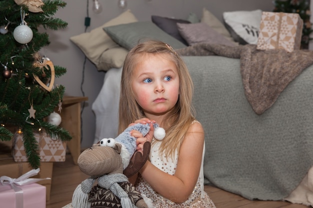 Une petite jolie fille avec des cadeaux de Noël assise près de l'arbre de Noël dans la chambre, concept du Nouvel An