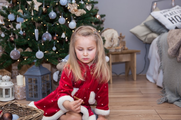 Une petite jolie fille avec des cadeaux de Noël assise près du sapin de Noël dans la chambre