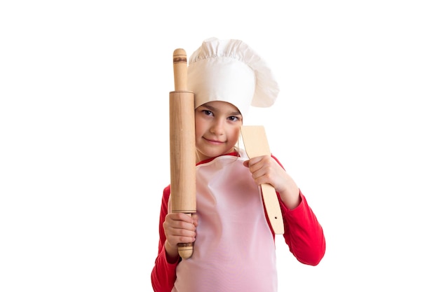 Photo petite jolie fille en chemise rouge avec tablier blanc et chapeau tenant un rouleau à pâtisserie sur fond blanc