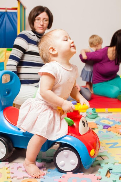 La petite jolie fille est assise sur le jouet de voiture