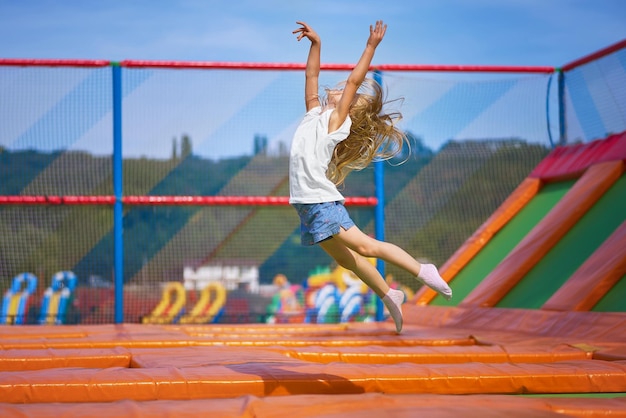 Petite jolie fille s'amusant en plein air Sauter sur le trampoline dans la zone des enfants Bonne fille sautant sur le trampoline jaune dans le parc d'attractions