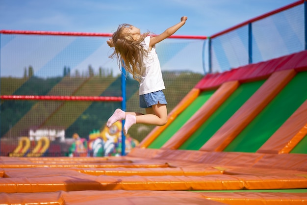 Photo petite jolie fille s'amuser en plein air. sauter sur trampoline en zone enfants. fille heureuse sautant sur le trampoline jaune dans le parc d'attractions