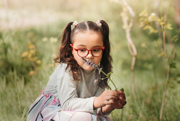 Une petite jolie fille tient une fleur lors d'une promenade dans le parc en été par une journée ensoleillée