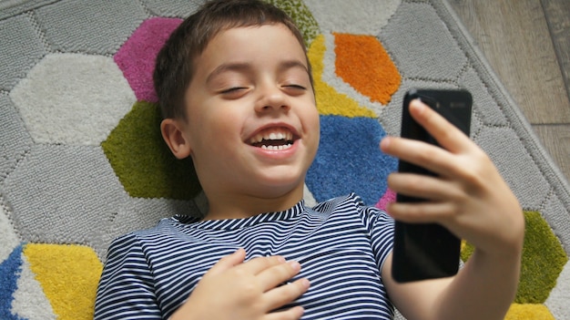 Petite main de garçon enfant souriant tenant un téléphone mobile ou un smartphone faisant selfie portrait photo ou conférence téléphonique