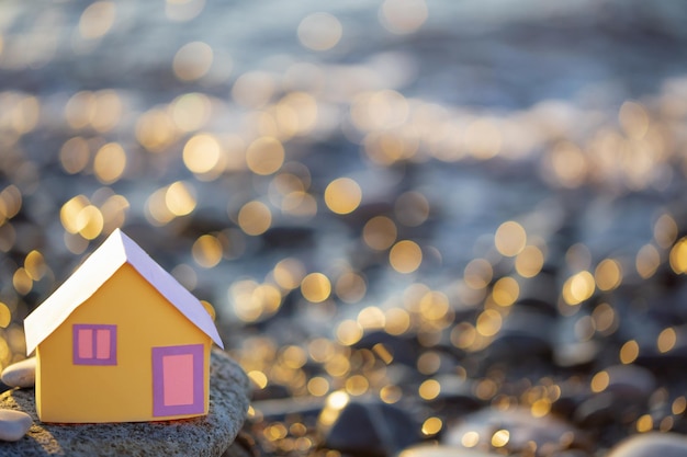 Une petite maison de papier sur fond de mer au coucher du soleil le concept de services immobiliers a