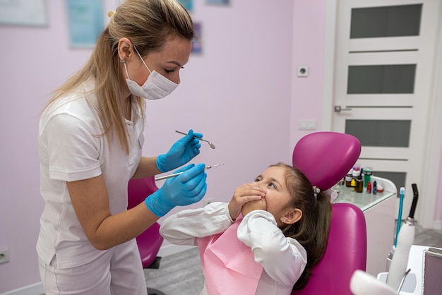 La petite patiente couvre sa bouche ses mains et ne permet pas au dentiste de regarder dans sa bouche