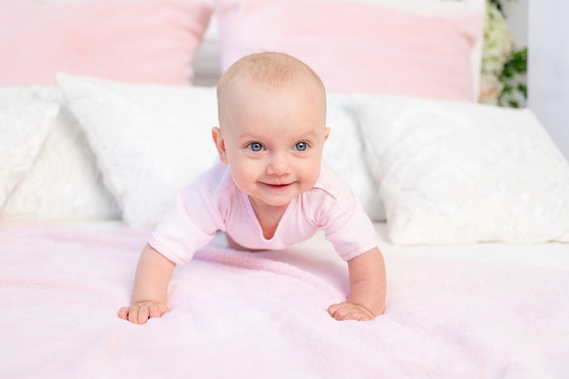 Petite petite fille de 6 mois rampant sur un lit rose et blanc, à l'écart, place pour le texte
