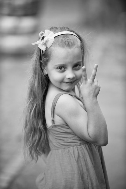 Petite petite fille ou enfant heureux mignon avec un adorable visage souriant et un arc dans les cheveux blonds en robe bleue en été en plein air sur fond flou