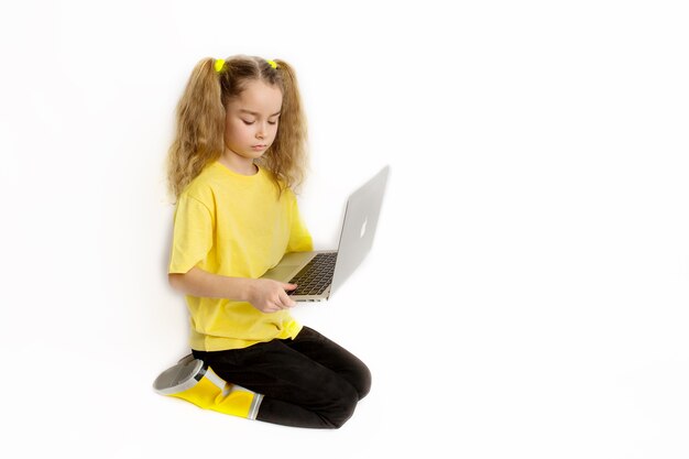 Petite petite fille européenne concentrée portant un t-shirt jaune assis devant un ordinateur vérifiant des tâches dans une salle de classe en ligne, concept d'apprentissage à distance en ligne.