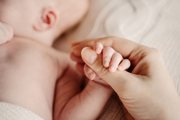 Petite poignée bébé nouveau-né dans la grande main de maman.