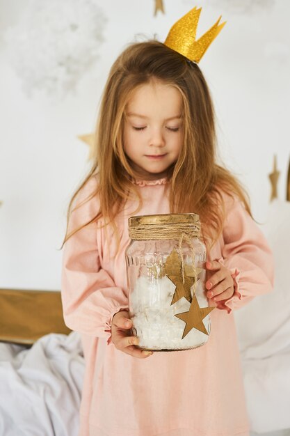 Petite princesse avec une baguette magique sur un lit dans un nuage sur fond blanc