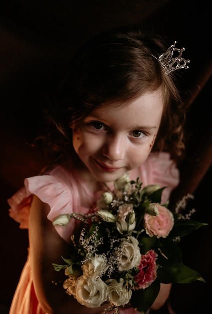 Petite princesse dans un bandeau avec une couronne tient un bouquet de fleurs sur un fond de tissu marron