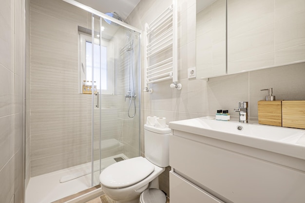 Petite salle de bains avec lavabo en porcelaine blanche sur une commode en bois avec armoires vitrées et cabine de douche vitrée