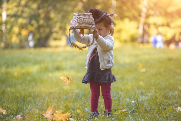 petite sorcière mignonne retourne un panier et verse des feuilles d'automne dans le parc.