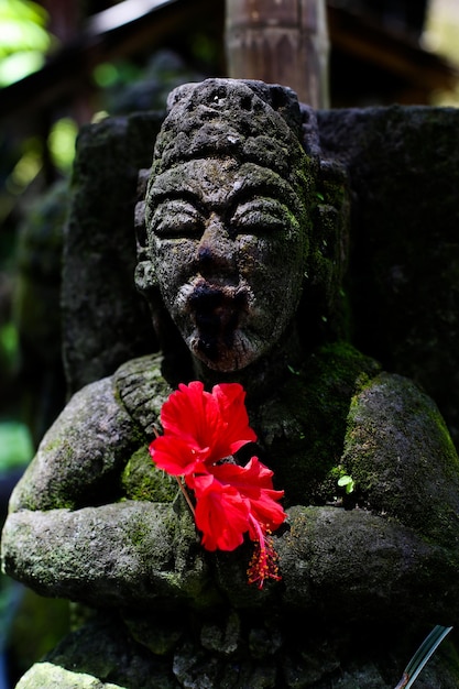 Petite statue en pierre dans le jardin de la maison avec une fleur rouge