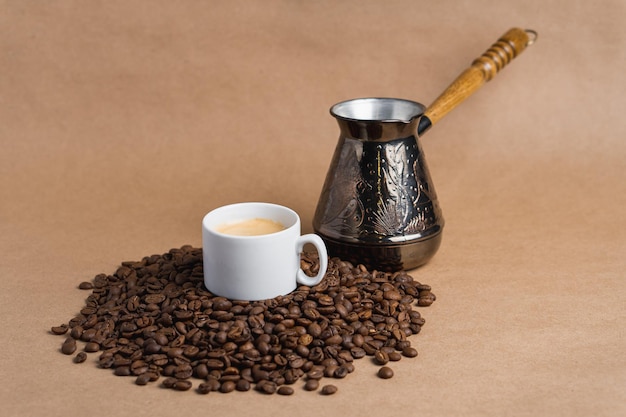 Petite tasse à café blanche avec crème expresso et cezve sur des haricots torréfiés sur fond marron Maquette