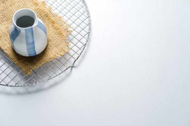 Une petite théière en céramique est photographiée avec une base en toile de jute sur un filet de sèche-gâteau