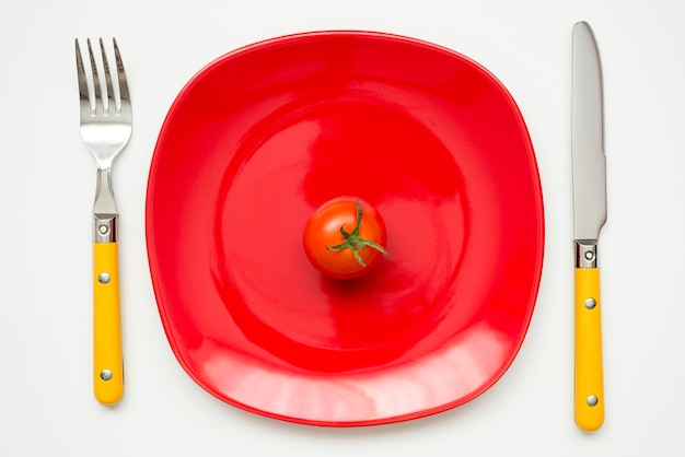 Petite tomate fraîche sur plaque rouge avec couverts