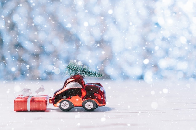 La petite voiture en gros plan porte un arbre de Noël et une boîte avec un cadeau, un concept de Noël et du nouvel an